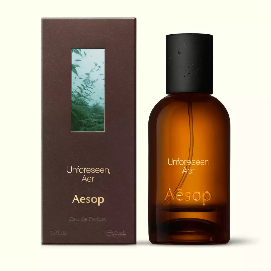 Amber glass Aesop Unforeseen Aer Eau de Parfum bottle beside its brown outer box on a white background.